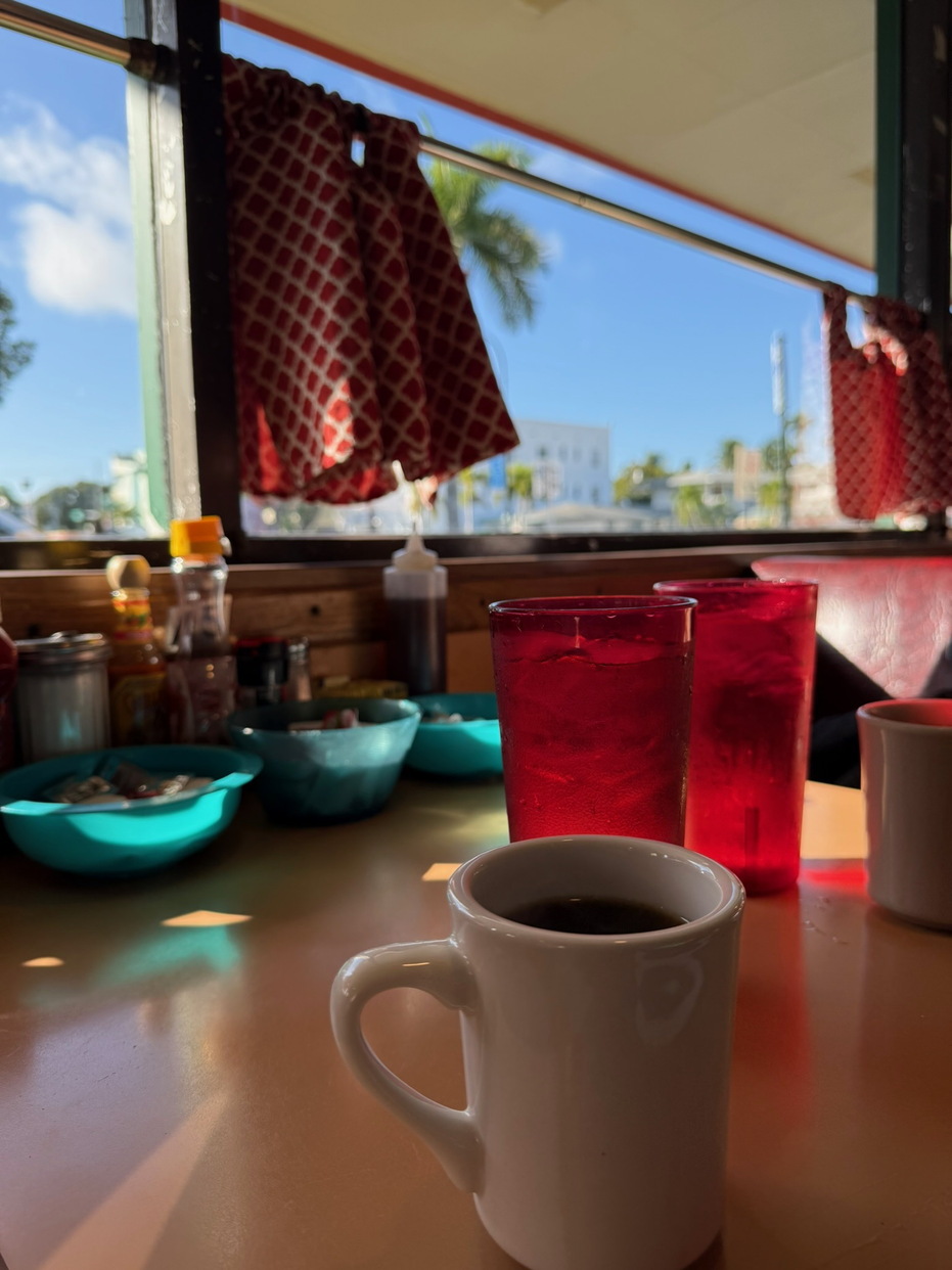 Kávéscsésze és piros poharak egy napfényes miami diner asztalán